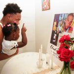 A man holding a toddler looks at a memorial photo