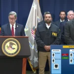 Joseph Nocella Jr speaking behind a podium, next to him is Kash Patel and other officials in suits.