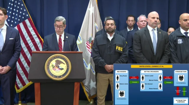 Joseph Nocella Jr speaking behind a podium, next to him is Kash Patel and other officials in suits.