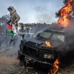 A protester holding a Malagasy flag jumps from a vandalised Gendarmerie armoured vehicle