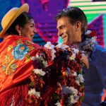 A Bolivian woman places a garland of flowers around Rodrigo Paz's neck on stage at a campaign event.