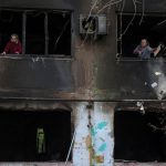 Residents remove broken glass from windows of an apartment building damaged by a Russian drone strike, amid Russia's attack on Ukraine, in the town of Shakhtarske in Dnipropetrovsk region, Ukraine October 19, 2025. REUTERS/Anatolii Stepanov
