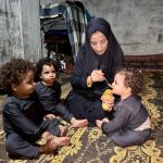Israa feeding the triplets on a worn plastic mat on the floor