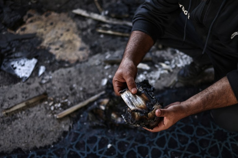 A Palestinian man holds a scorched fragment of a Koran page inside the Hajja Hamida Mosque after it was reportedly set on fire and vandalised by Israeli settlers in the Palestinian village of Deir Istiya, near Salfit in the Israeli-occupied West Bank, on November 13, 2025.