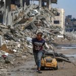 A Palestinian boy collects scrap metal from a street filled with debris.