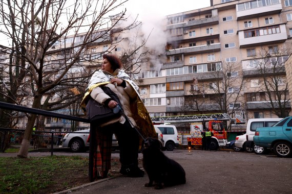 A woman stands with a dog next to the site of a damaged apartment building.